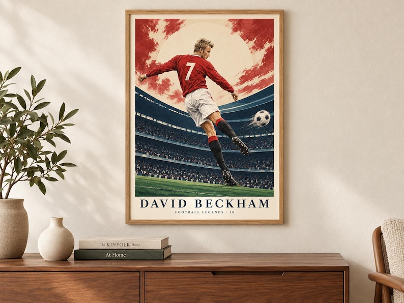 May include: A framed poster featuring a soccer player wearing a red jersey with the number 7 and white shorts, kicking a soccer ball in a stadium. The text DAVID BECKHAM FOOTBALL LEGENDS 10 is printed at the bottom against a red and white sky background.