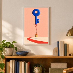 May include: A framed wall art print featuring a surreal illustration of a large, glossy blue key floating like a balloon, tethered by a thin red string to a small, yellow house with a red roof, set against a soft peach background.