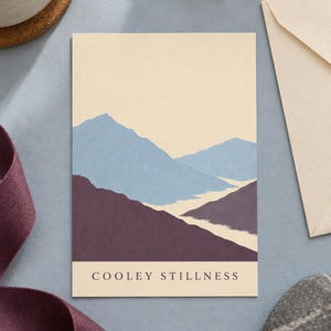 May include: A rectangular greeting card featuring a stylized mountain landscape illustration in shades of light blue and deep purple against a cream background. The text "COOLEY STILLNESS" is printed in a dark serif font at the bottom of the card.