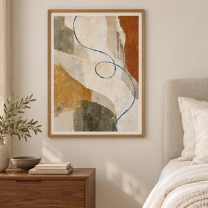 Puede incluir: Una impresi&oacute;n de arte mural abstracto enmarcada que presenta formas org&aacute;nicas en capas en tonos crema, terracota, amarillo mostaza y verde oliva. Una l&iacute;nea &uacute;nica, fina y de color azul oscuro se curva y forma un bucle en el centro de la composici&oacute;n, contrastando con los bloques de colores terrosos y texturizados.