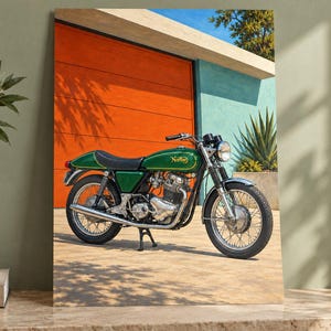 May include: A green Norton motorcycle with a black seat, chrome exhaust, and wire-spoke wheels parked on a paved surface. The motorcycle features a classic fuel tank design with gold lettering and is positioned in front of a bright orange wall.