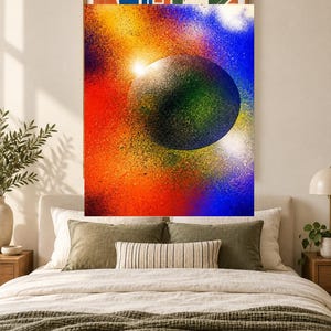 Op de afbeelding: Een rechthoekige wandkunstprint met een grote, donkere, getextureerde bol gecentreerd tegen een levendige, met spuitverf bewerkte achtergrond van gemengd rood, oranje, geel en blauw, met een heldere witte lichtvlek nabij de rand.
