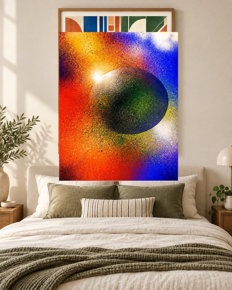 Op de afbeelding: Een rechthoekige wandkunstprint met een grote, donkere, getextureerde bol gecentreerd tegen een levendige, met spuitverf bewerkte achtergrond van gemengd rood, oranje, geel en blauw, met een heldere witte lichtvlek nabij de rand.