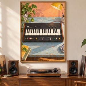 May include: A framed wall art print depicting a black Korg Monologue synthesizer with white keys, knobs, and sliders, resting on a weathered blue wooden table. The scene includes a yellow lamp, a potted plant, and books, all captured in a warm, sunlit aesthetic.