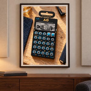 Op de afbeelding: Een zwarte Teenage Engineering PO-128 pocket operator synthesizer met een digitaal LCD-scherm met een onderzeebootafbeelding, twee blauwe draaiknoppen en een raster van zestien ronde knoppen met blauwe labels op een zwarte printplaat.