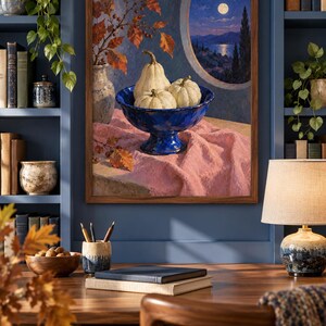 May include: A framed oil painting depicting a blue pedestal bowl filled with three white pumpkins, resting on a pink cloth. Beside the bowl is a vase with autumn leaves. The background shows a circular window view of a moonlit lake and hills.