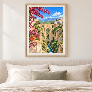 Pu&ograve; includere: Una stampa d'arte incorniciata che raffigura un ponte in pietra che attraversa una profonda gola con un fiume sottostante. La scena presenta fiori di bouganville rosa brillante in primo piano, edifici bianchi sulla scogliera e cielo blu.