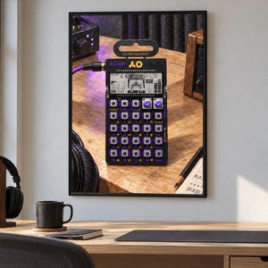 May include: A black Teenage Engineering PO-20 Arcade pocket operator synthesizer featuring a monochrome LCD screen, purple buttons, and a purple audio cable connected to the side. The device displays the text arcade and pocket operator.