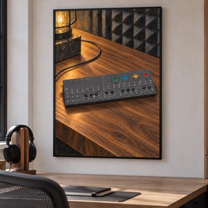Op de afbeelding: Een rechthoekige donkergrijze elektronische synthesizer met een raster van kleine ronde knoppen, een rij van vier grotere gekleurde knoppen in groen, blauw, geel en rood, en een enkele goudkleurige knop aan de linkerkant, weergegeven als wandkunst.