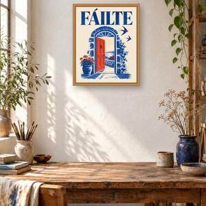 Puede incluir: Una l&aacute;mina de arte mural enmarcada que muestra la palabra F&Aacute;ILTE en azul sobre una ilustraci&oacute;n de un arco de piedra con una puerta roja brillante, detalles florales azules y dos p&aacute;jaros volando sobre un fondo crema, en un marco dorado fino.