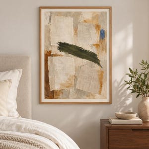 May include: A framed abstract wall art print featuring layered, torn-paper-style rectangular shapes in shades of beige, cream, and tan, accented by a bold, horizontal dark green brushstroke and a small patch of vibrant blue paint.