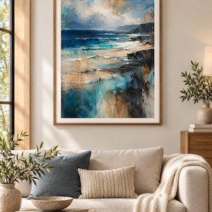 K&ouml;nnte beinhalten: Ein gerahmter Kunstdruck mit einer abstrakten K&uuml;stenlandschaft, die tiefblaue Meereswellen, sandfarbene K&uuml;stenlinien und dunkle Felsklippen unter einem bew&ouml;lkten Himmel zeigt, eingefasst in einen schlichten Holzrahmen mit wei&szlig;em Passepartout.