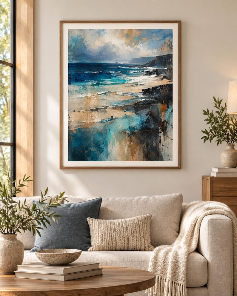 K&ouml;nnte beinhalten: Ein gerahmter Kunstdruck mit einer abstrakten K&uuml;stenlandschaft, die tiefblaue Meereswellen, sandfarbene K&uuml;stenlinien und dunkle Felsklippen unter einem bew&ouml;lkten Himmel zeigt, eingefasst in einen schlichten Holzrahmen mit wei&szlig;em Passepartout.