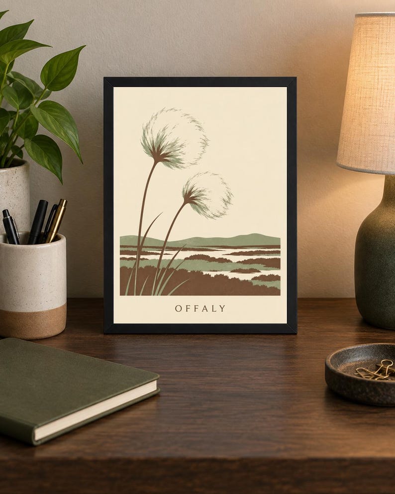 May include: A framed art print featuring a cream background with two fluffy white seed heads on long brown stems in the foreground. Below, a stylized landscape of green and brown marshland is depicted. The word OFFALY is printed in black at the bottom.