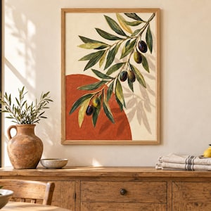 May include: A framed wall art print featuring a painted olive branch with dark green leaves and ripe olives hanging over a large, solid terracotta-colored circle against a cream-colored background, enclosed in a light-toned wooden frame.