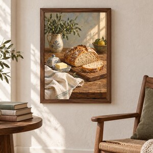 Peut inclure: Une impression d'art mural encadr&eacute;e repr&eacute;sentant une nature morte rustique sur une table en bois. L'image montre une miche de pain au levain croustillant, une tranche de pain, un beurrier en c&eacute;ramique avec une motte de beurre et un pichet.