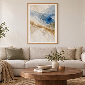 Puede incluir: Una impresi&oacute;n de arte abstracto enmarcada que presenta pinceladas texturizadas en tonos azul profundo, beige arena y blanco suave. La obra de arte se exhibe en un marco de madera clara, mostrando una composici&oacute;n fluida y en capas.