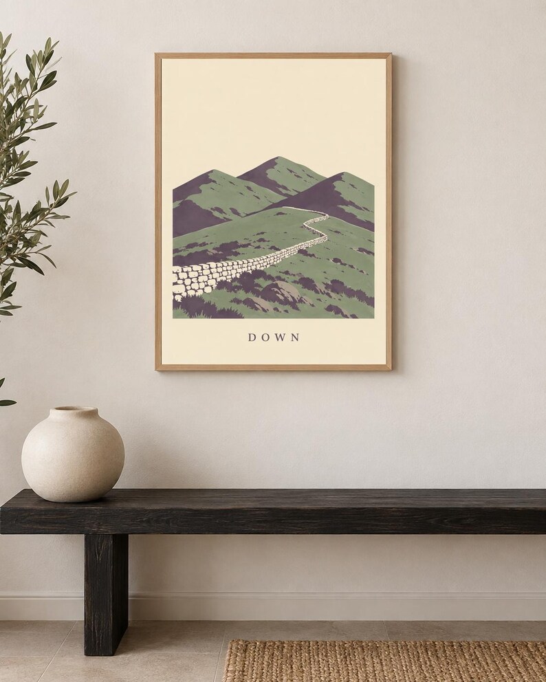 Pu&ograve; includere: Una stampa artistica incorniciata che presenta un'illustrazione paesaggistica stilizzata di montagne verdi e un muro di pietra che si snoda lungo un sentiero. La parola DOWN &egrave; stampata in lettere maiuscole scure al centro del fondo color crema.