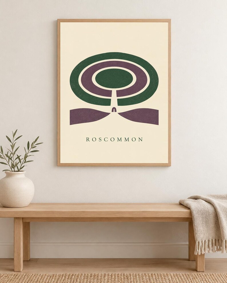 May include: A framed wall art print featuring a cream background with a centred graphic design of concentric dark green and purple oval shapes. Below the shapes, the text ROSCOMMON is printed in a simple, dark, sans-serif font.