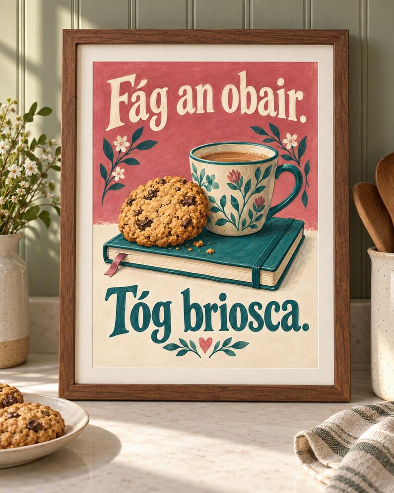 Pu&ograve; includere: Una stampa artistica incorniciata raffigurante un biscotto con gocce di cioccolato su un libro verde acqua accanto a una tazza a motivi floreali. Il testo recita F&aacute;g an obair. T&oacute;g briosca. Lo sfondo &egrave; diviso tra rosso spento e crema.