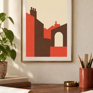 K&ouml;nnte beinhalten: Ein gerahmter Wandkunstdruck mit einer geometrischen Architekturillustration von Geb&auml;uden in den Farben Dunkelbraun, leuchtendes Orange und Creme. Die Komposition zeigt stilisierte D&auml;cher, Schornsteine und einen einzelnen Torbogen vor einem hellen Hintergrund.