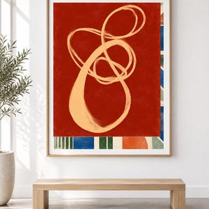 Pode incluir: Uma impress&atilde;o de arte de parede retangular emoldurada com um fundo vermelho profundo e um grande desenho de linha cont&iacute;nua em bege claro. A borda inferior exibe um padr&atilde;o de listras verticais azuis e verdes ao lado de um c&iacute;rculo laranja.