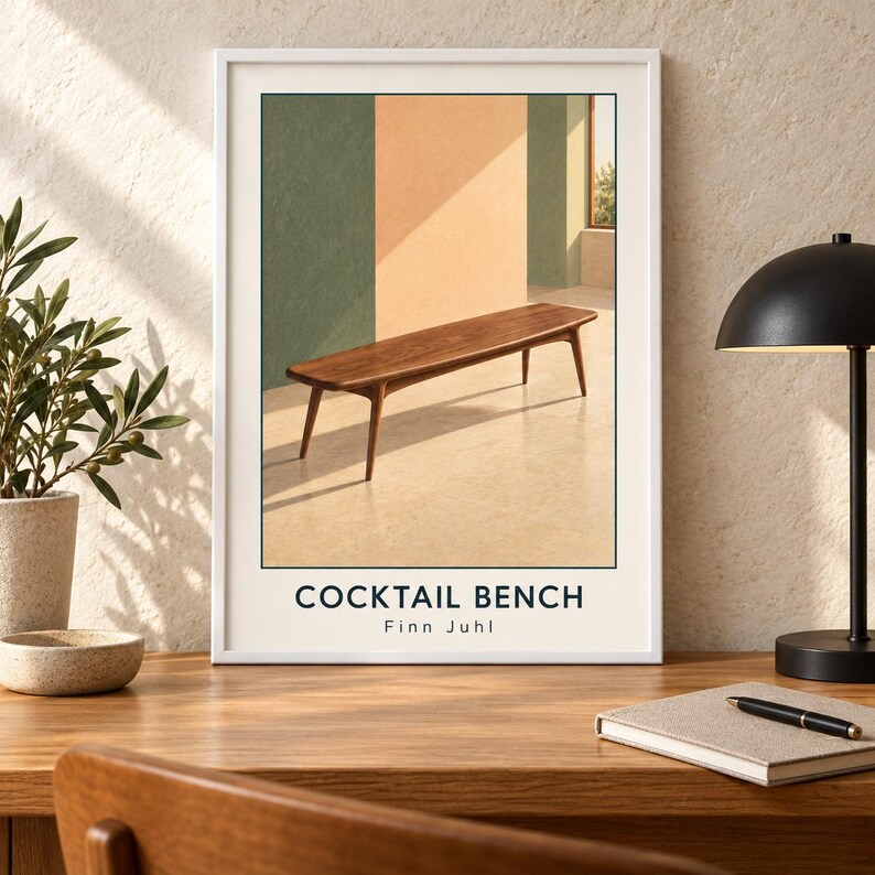 May include: A framed art print featuring a wooden bench with tapered legs set against a background of green and peach-colored walls. The text COCKTAIL BENCH and Finn Juhl is printed in dark blue at the bottom of the white-bordered poster.