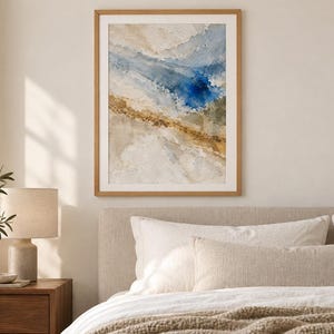 Puede incluir: Una impresi&oacute;n de arte mural abstracto enmarcada que presenta pinceladas texturizadas en tonos azul profundo, beige arena y blanco apagado. La obra de arte est&aacute; encerrada en un marco de madera de tono claro, mostrando una composici&oacute;n de colores.