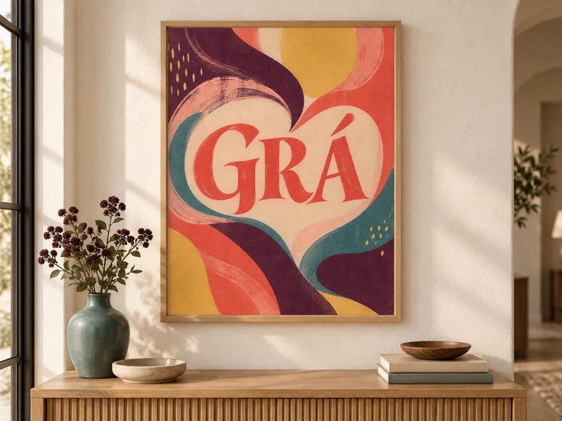 May include: A rectangular wall art print in a light wood frame featuring the word GR&Aacute; in large red letters centred within a cream-coloured heart shape, surrounded by abstract flowing shapes in shades of yellow, pink, teal, and deep purple.