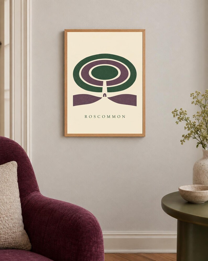 May include: A framed wall art print featuring a cream background with a central graphic design of concentric green and purple oval shapes. Below the shapes, a vertical line leads to a purple base, with the text ROSCOMMON printed in black.