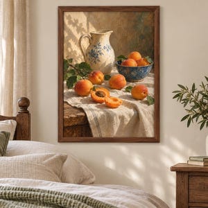 May include: A framed wall art print depicting a still life scene with a cream-colored ceramic pitcher featuring blue floral patterns, a blue bowl filled with fresh orange apricots, and several loose apricots resting on a textured white cloth.