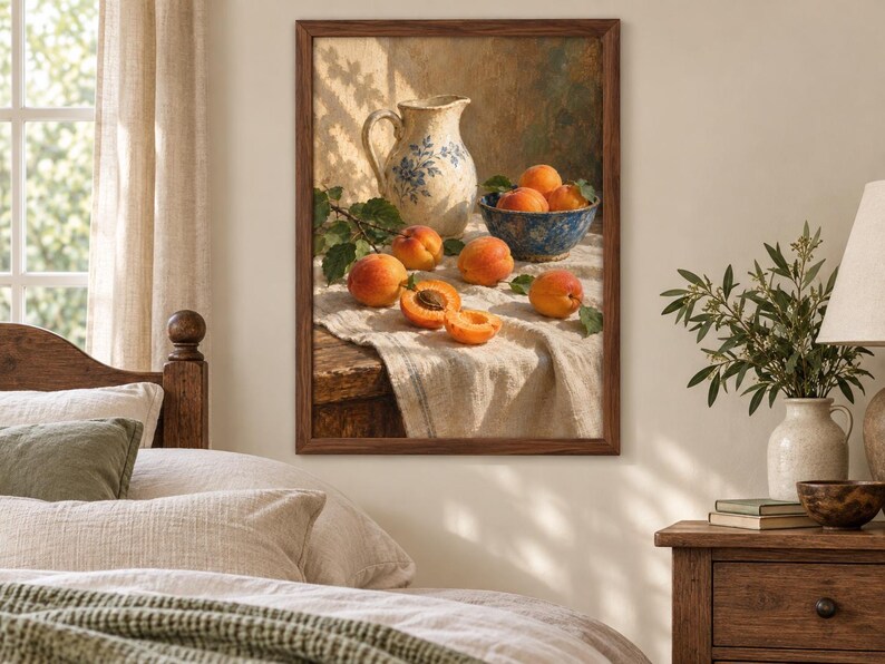 May include: A framed wall art print depicting a still life scene with a cream-colored ceramic pitcher featuring blue floral patterns, a blue bowl filled with fresh orange apricots, and several loose apricots resting on a textured white cloth.