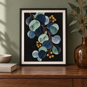 May include: A framed wall art print featuring a botanical illustration of a eucalyptus branch with rounded leaves in shades of dark blue, teal, and light green against a solid black background, accented by small clusters of golden-brown seed pods.