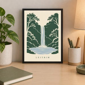 K&ouml;nnte beinhalten: Ein gerahmter Kunstdruck mit einer stilisierten Illustration eines Wasserfalls, der in ein Becken st&uuml;rzt, umgeben von dunkelgr&uuml;nen B&auml;umen und Blattwerk. Der Hintergrund ist cremefarben und das Wort LEITRIM ist unten mittig in Schwarz gedruckt.