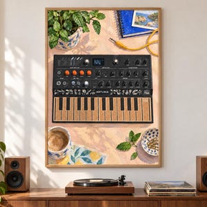 May include: A framed art print featuring a black Arturia MicroFreak synthesizer with orange knobs and a textured keyboard. The illustration includes a potted plant, a blue notebook, a yellow audio cable, a coffee mug, and a small bowl of paperclips.