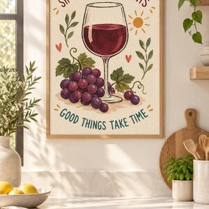May include: A framed wall art print featuring a glass of red wine, a cluster of purple grapes, and green leaves. The text reads SIP THE SWEET MOMENTS at the top and GOOD THINGS TAKE TIME at the bottom, accented by small red hearts and a yellow sun.