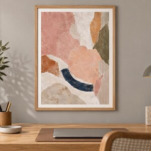 May include: A framed abstract wall art print featuring organic, layered shapes in muted tones of dusty pink, terracotta, olive green, white, and a deep navy blue curved accent, all enclosed within a light-toned wooden frame.