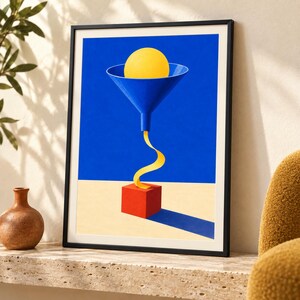 Op de afbeelding: Een ingelijste kunstdruk met een blauwe trechter die een gele bol bevat. Een geel lint stroomt vanuit de trechter in een rode kubus op een beige ondergrond tegen een effen blauwe achtergrond. De compositie gebruikt gedurfde geometrische vormen.