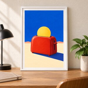 May include: A framed art print featuring a bright red toaster centered on a light beige surface against a deep blue sky. A large, solid yellow circle emerges from the toaster slot, casting a sharp, dark blue shadow across the ground.