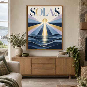 May include: A rectangular framed wall art print featuring the word SOLAS in large dark blue letters at the top. The artwork depicts a stylized sun rising over dark blue ocean waves with radiating beams of light in gold, blue, and lavender.