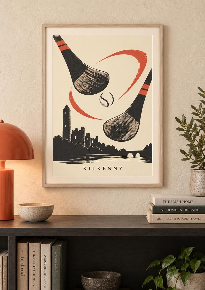 Peut inclure: Une affiche encadr&eacute;e repr&eacute;sentant une illustration stylis&eacute;e de deux crosses de hurling et une balle au-dessus de la silhouette du ch&acirc;teau et de la tour ronde de Kilkenny. Le design utilise un fond cr&egrave;me avec des accents noirs et orange et le texte KILKENNY.
