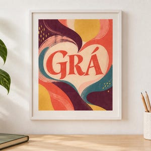 May include: A framed wall art print featuring the word GR&Aacute; in large red serif letters centred within a cream-coloured heart shape. The background consists of abstract, flowing organic shapes in shades of deep purple, coral, yellow, and teal.