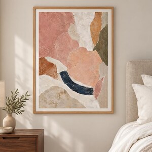 May include: A framed abstract wall art print featuring organic, layered shapes in a palette of dusty pink, terracotta, cream, olive green, and a deep navy blue curved accent. The composition has a textured, collage-like appearance with soft edges.