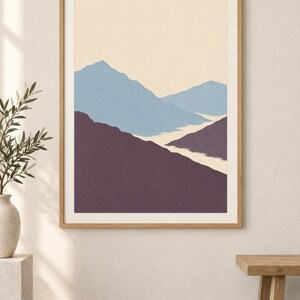 May include: A framed wall art print featuring a stylized mountain landscape with layered peaks in shades of muted blue and deep purple against a pale cream sky. The artwork is enclosed in a light-toned wooden frame with a white mat border.