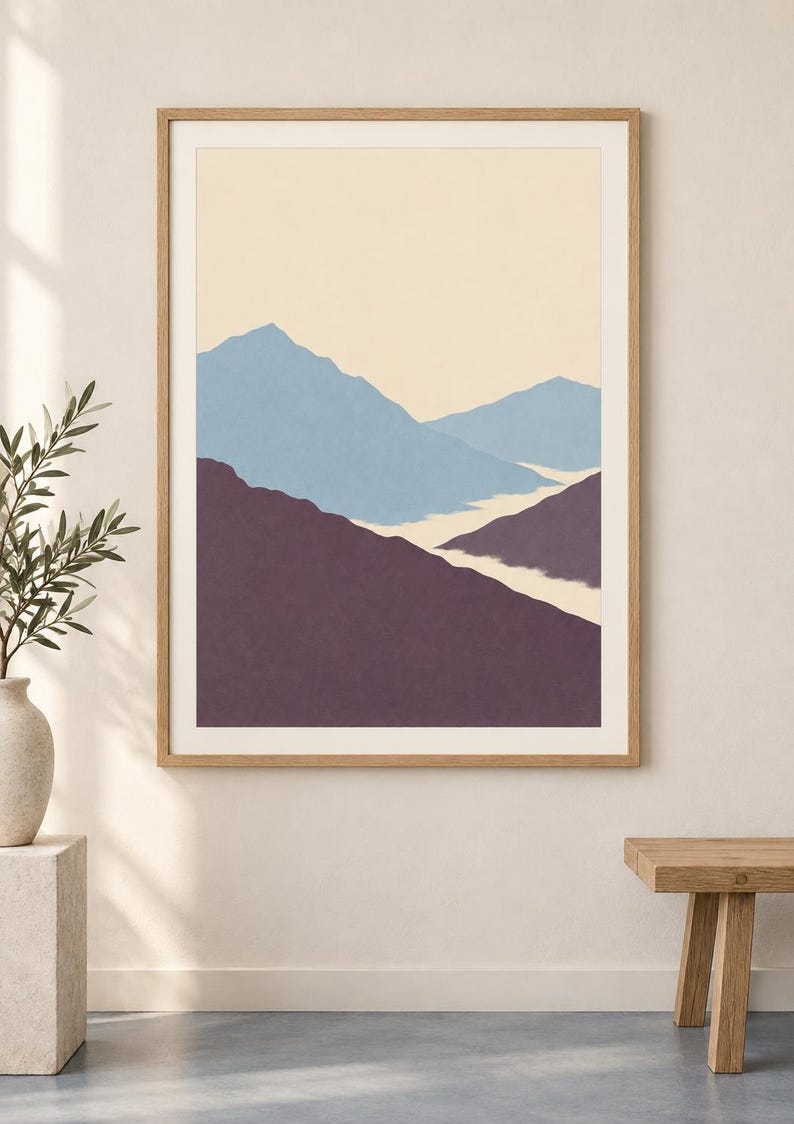 May include: A framed wall art print featuring a stylized mountain landscape with layered peaks in shades of muted blue and deep purple against a pale cream sky. The artwork is enclosed in a light-toned wooden frame with a white mat border.