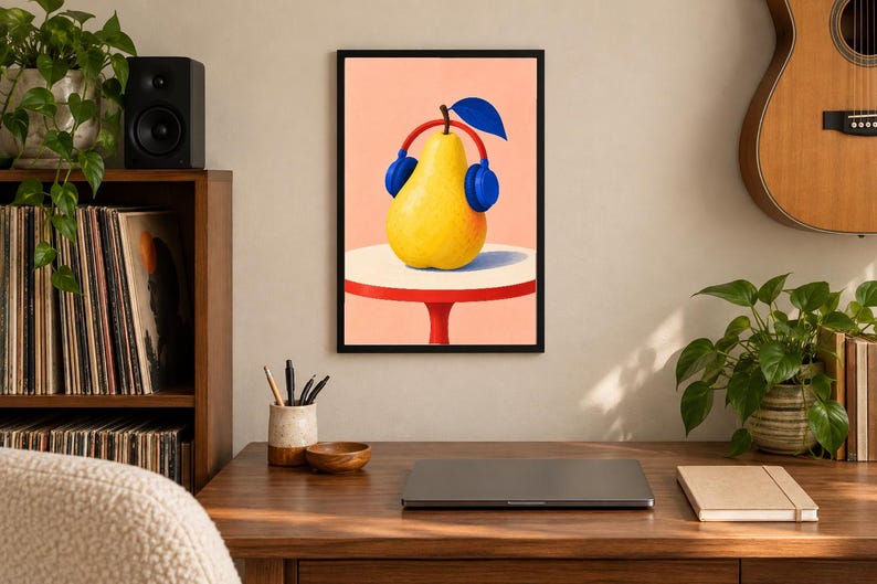 May include: A framed wall art print featuring a yellow pear wearing blue headphones, set against a light peach background. The pear rests on a white circular table with a red base. The illustration uses bold colours and clean lines to depict the fruit.