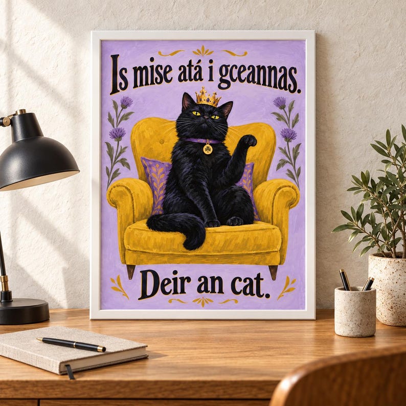 May include: A framed wall art print featuring a black cat wearing a gold crown and a purple collar with a clover charm, sitting on a yellow armchair against a light purple background with floral accents and the text Is mise at&aacute; i gceannas. Deir an cat.
