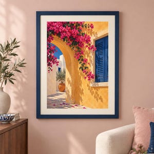 May include: A framed wall art print depicting a Mediterranean scene with a yellow stucco wall, a bright blue shuttered window, and vibrant pink bougainvillea flowers cascading over a stone archway leading to a sunlit courtyard with a potted plant.