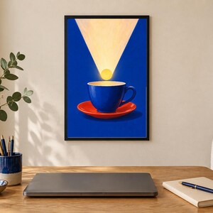 Puede incluir: Una impresi&oacute;n de arte mural enmarcada que muestra una taza de caf&eacute; azul sobre un plato rojo contra un fondo azul intenso. Un haz de luz amarillo brillante brilla hacia abajo desde la parte superior del marco, iluminando un c&iacute;rculo amarillo.
