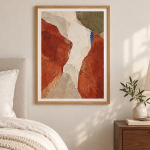 May include: A framed abstract wall art print featuring a textured composition of deep terracotta red, muted olive green, off-white, and light gray shapes. The artwork is enclosed in a simple light-toned wooden frame with a white mat border.